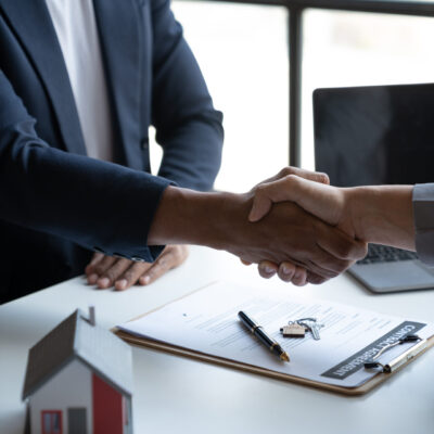 Two young Asian businessmen shake hands after signing a contract to invest in a village project. real estate, with businesswomen joining in showing joy and clapping in the office.